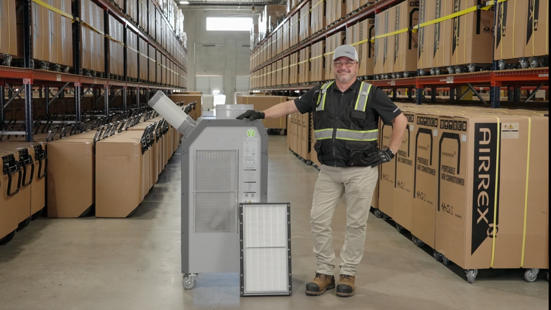 A Temp-Air technician in a high-density warehouse standing with an Airrex HSC-18R 1.5-ton portable spot cooler and a detached high-efficiency HEPA filter, demonstrating industrial climate control solutions for cleanroom and medical-grade air filtration applications.