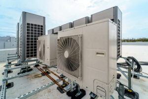 A massive array of fixed commercial air conditioning units drawing high energy on a building rooftop, illustrating the excessive operational costs of central HVAC overcooling. This highlights the financial drain of cooling entire vacant zones and showcases why facilities are switching to targeted portable spot coolers and portable AC units from Temp-Air to save money.