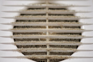 A dirty, dusty commercial HVAC ventilation grill with a clogged air filter, highlighting the need for a portable air scrubber to combat sick building syndrome.