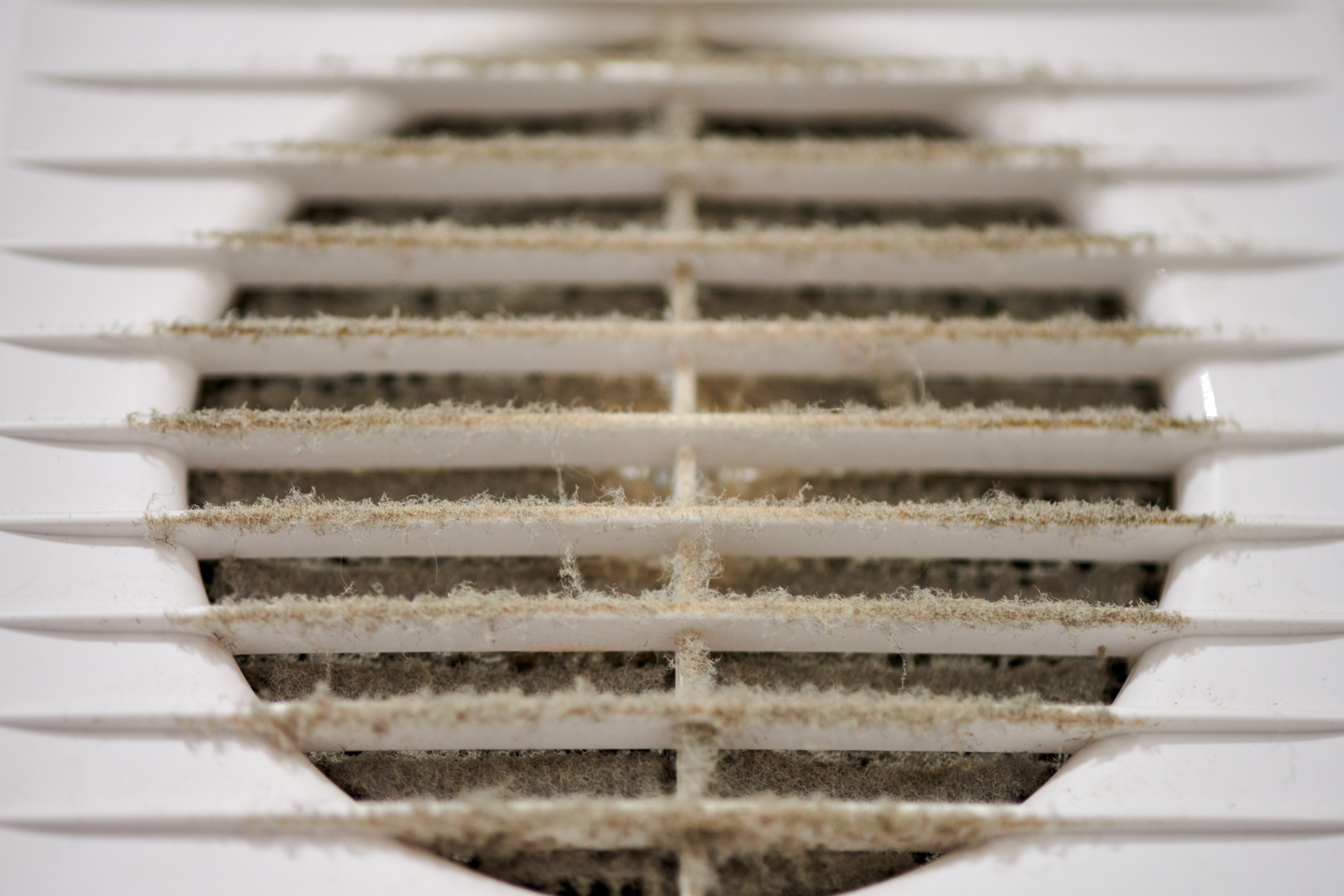 A dirty, dusty commercial HVAC ventilation grill with a clogged air filter, highlighting the need for a portable air scrubber to combat sick building syndrome.